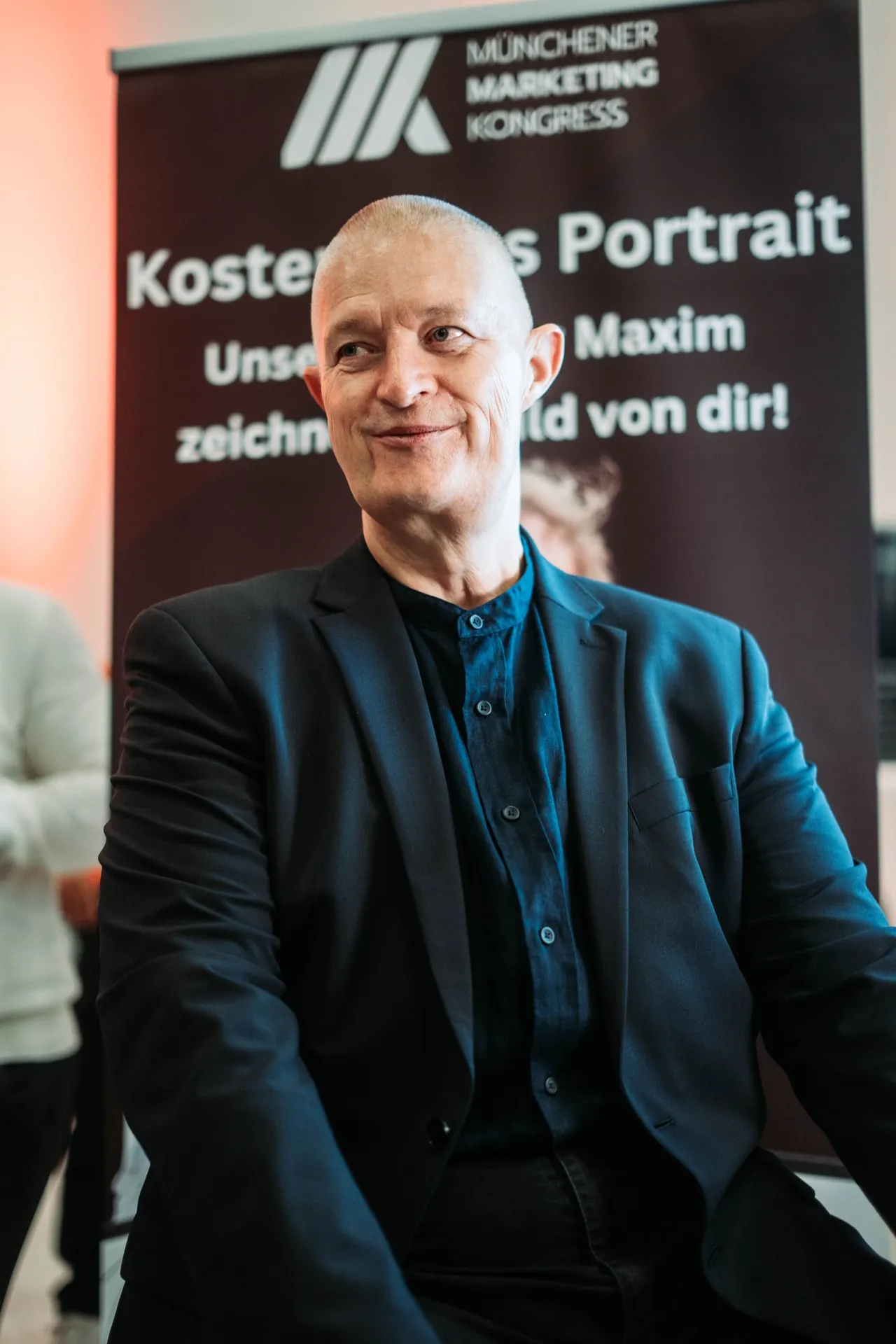 Joschi Haunsperger vor einer Fotowand des Münchner Marketing Kongresses