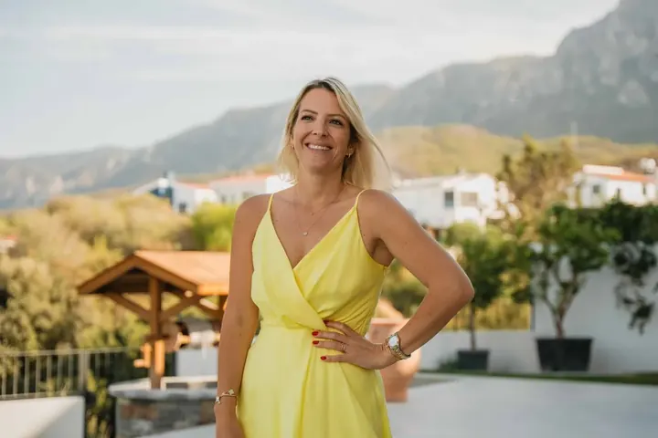 Susanne Rey im gelben Kleid auf einer Terrasse mit Bergblick
